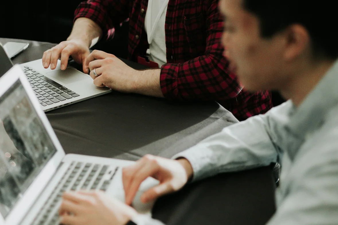Two people working at a table with open laptops