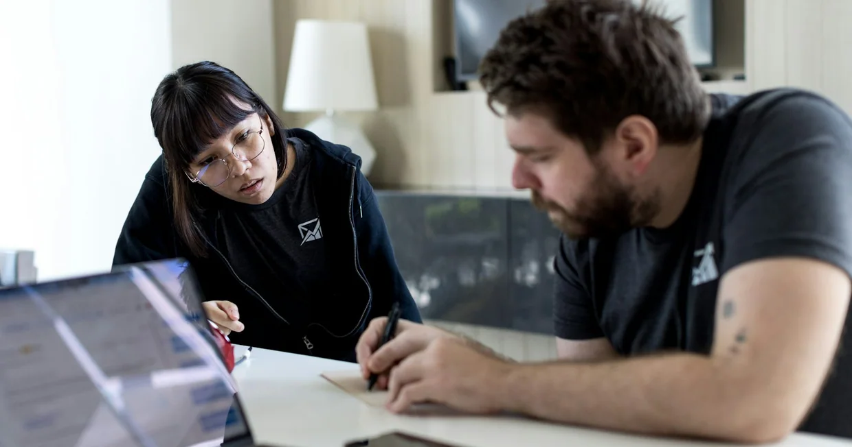 A man and a woman sitting at a table with a laptop between them in discussion