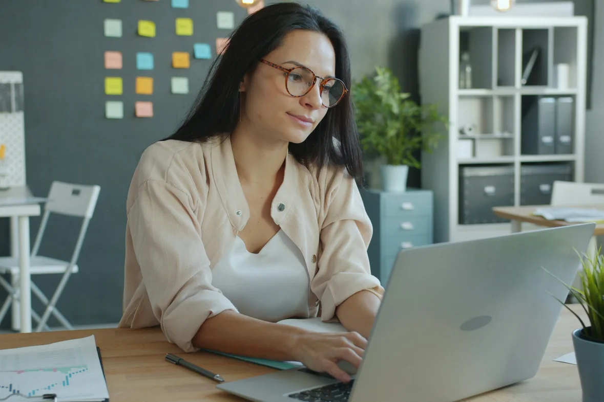 A person working at a laptop in an office, a wall of coloured sticky notes behind them