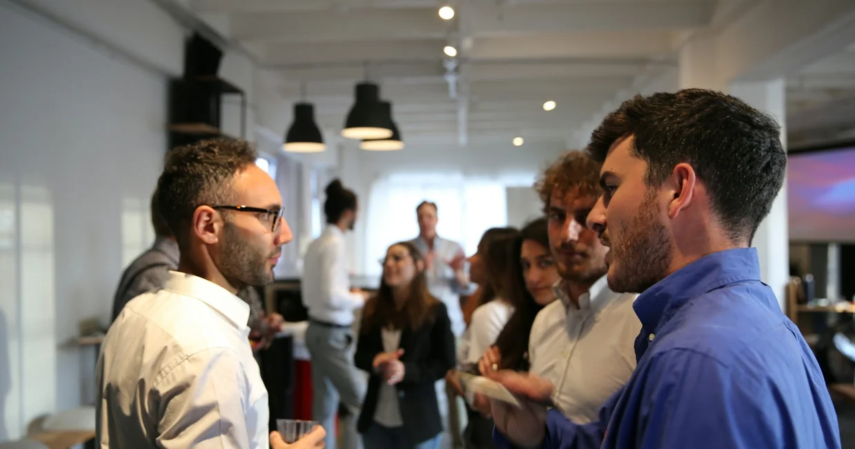 A professional networking event in a bright open room, people standing in small groups in conversation