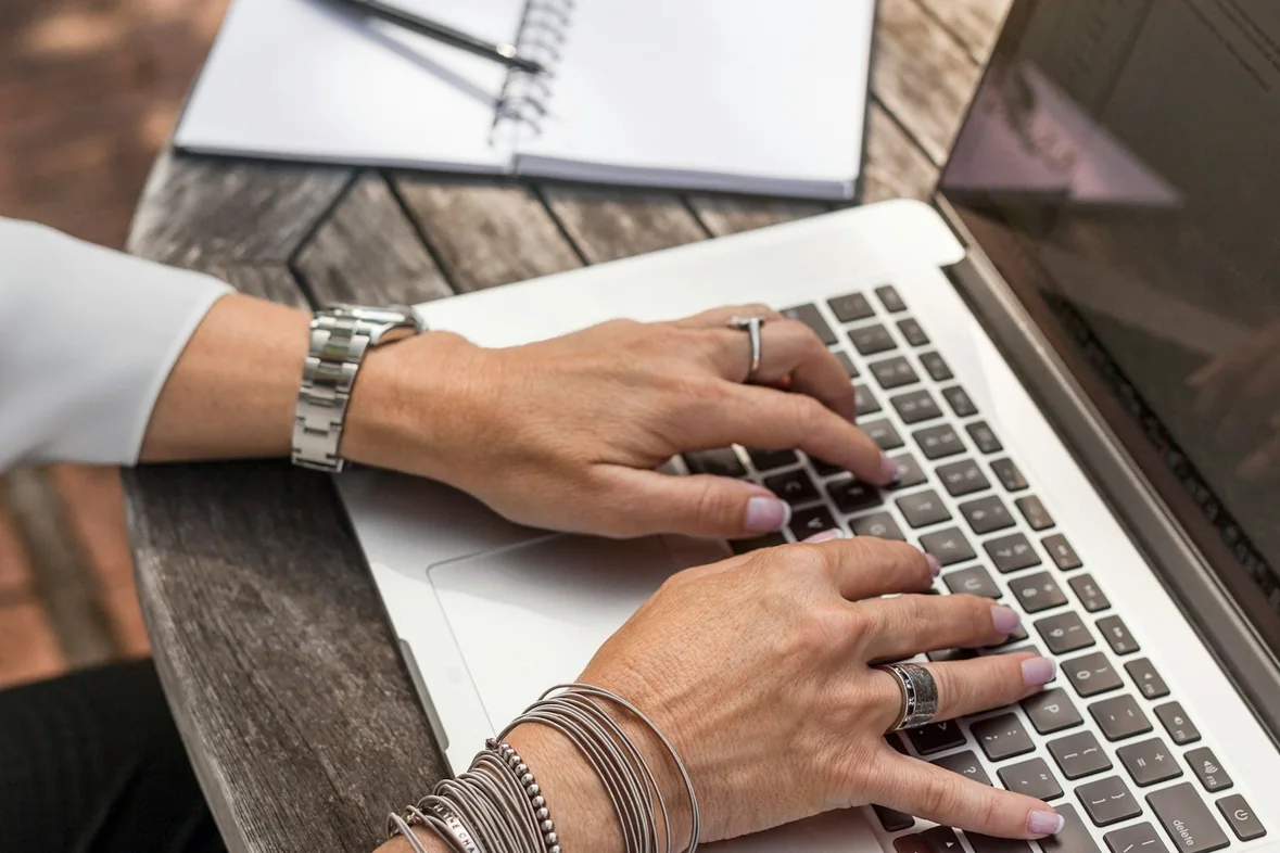 Hands typing on a laptop resting on a brown wooden table