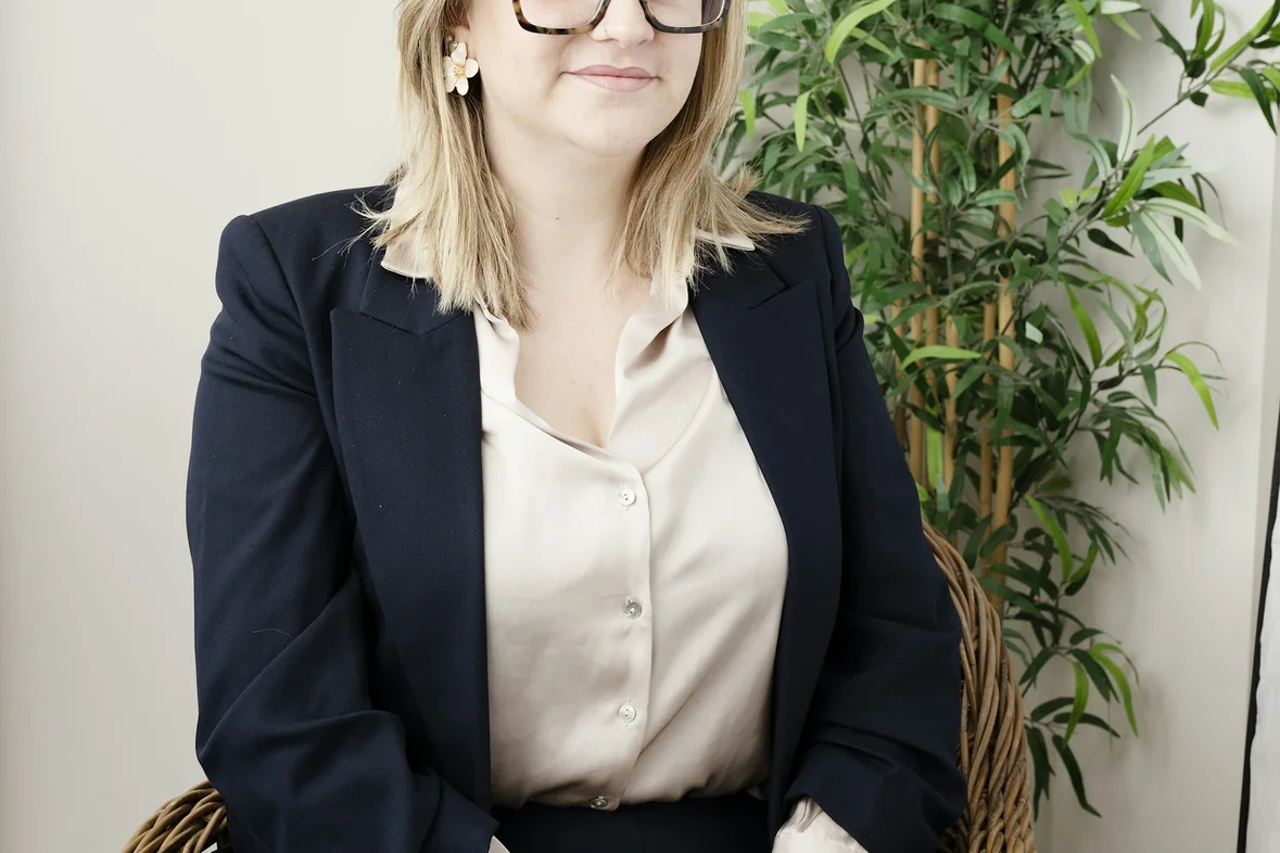 A professional portrait of a woman in a dark suit seated against a light background