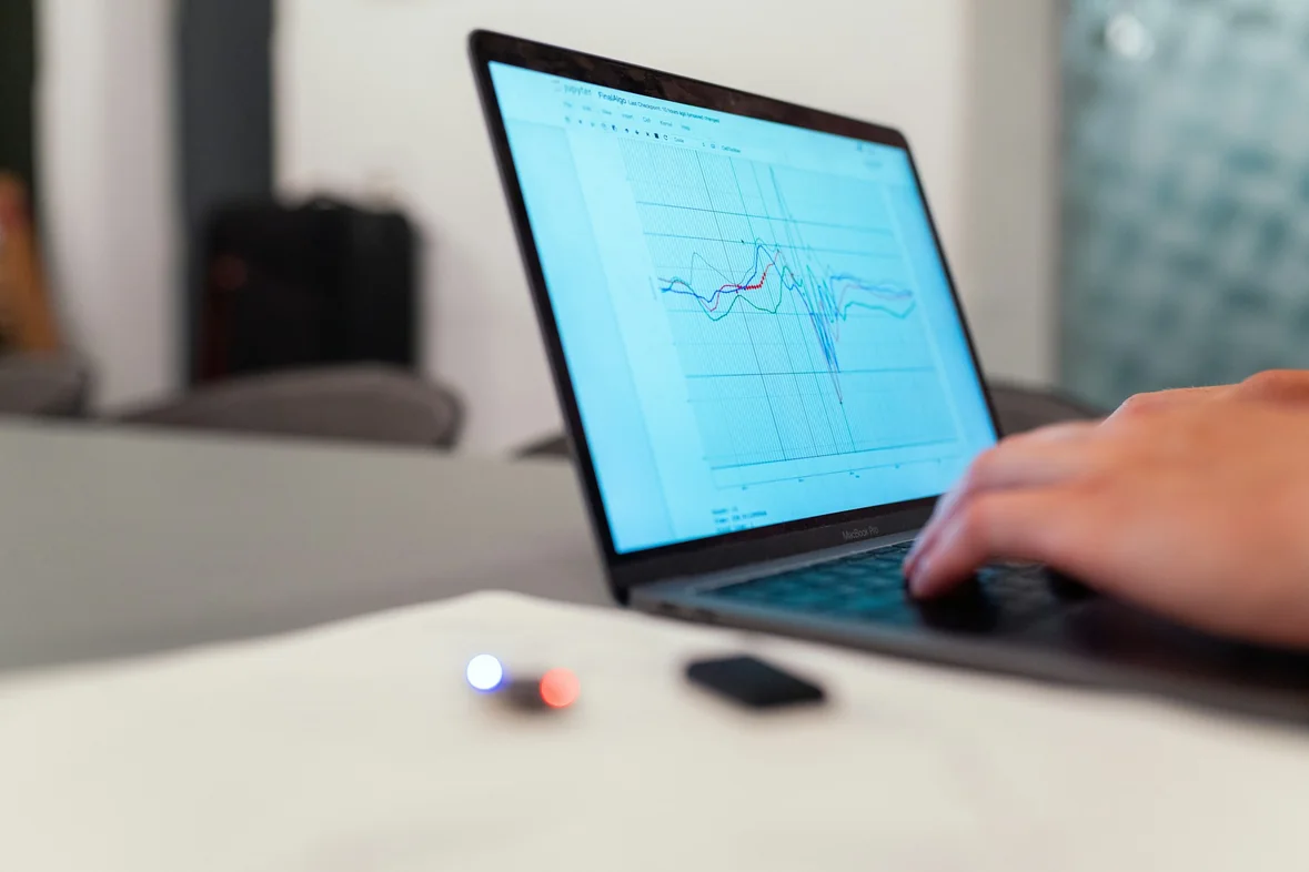 A person working at a laptop displaying a line chart on a pale desk