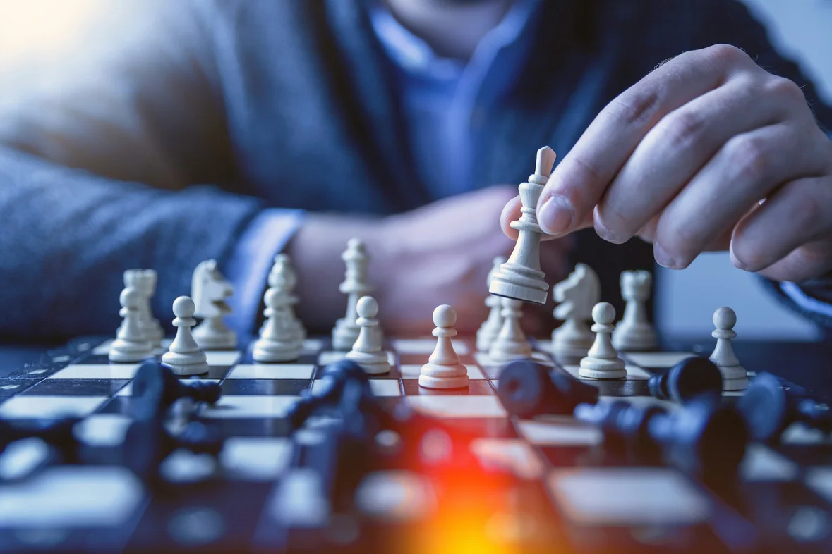 A hand moving a piece on a chessboard, the remaining pieces in soft focus behind it