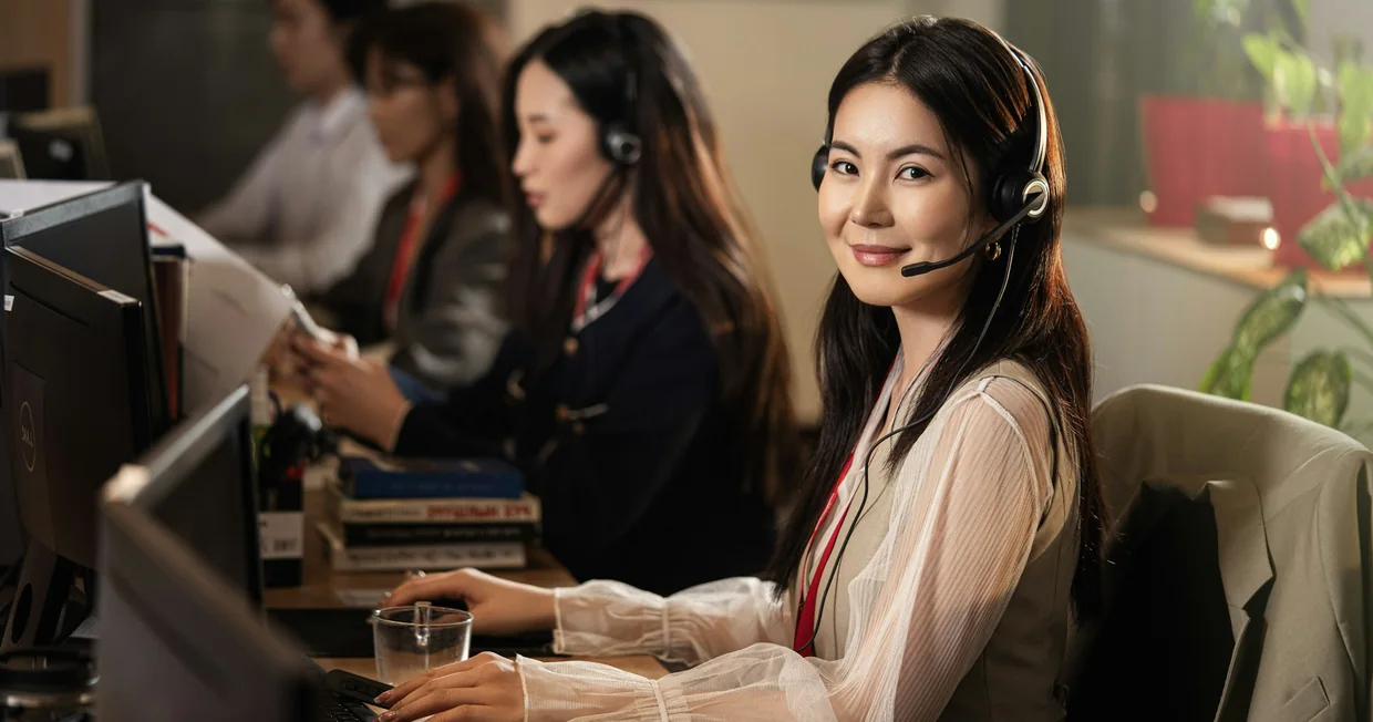 A row of people wearing headsets working at computers in a bright open office