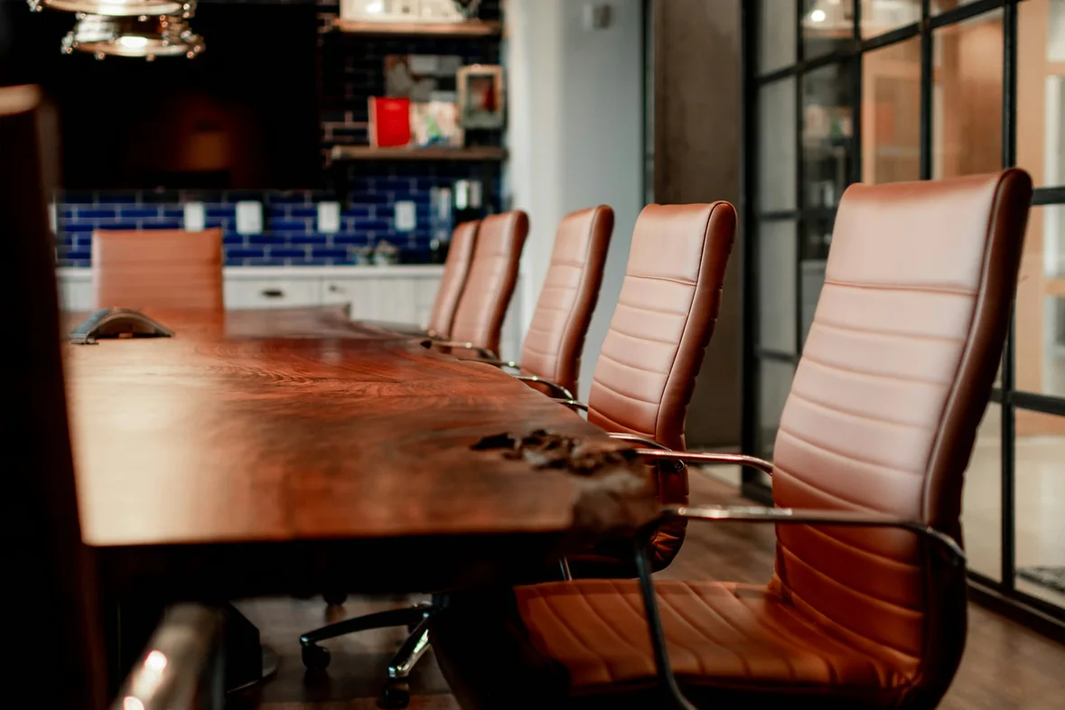 An empty boardroom with a long wooden table and a row of leather chairs
