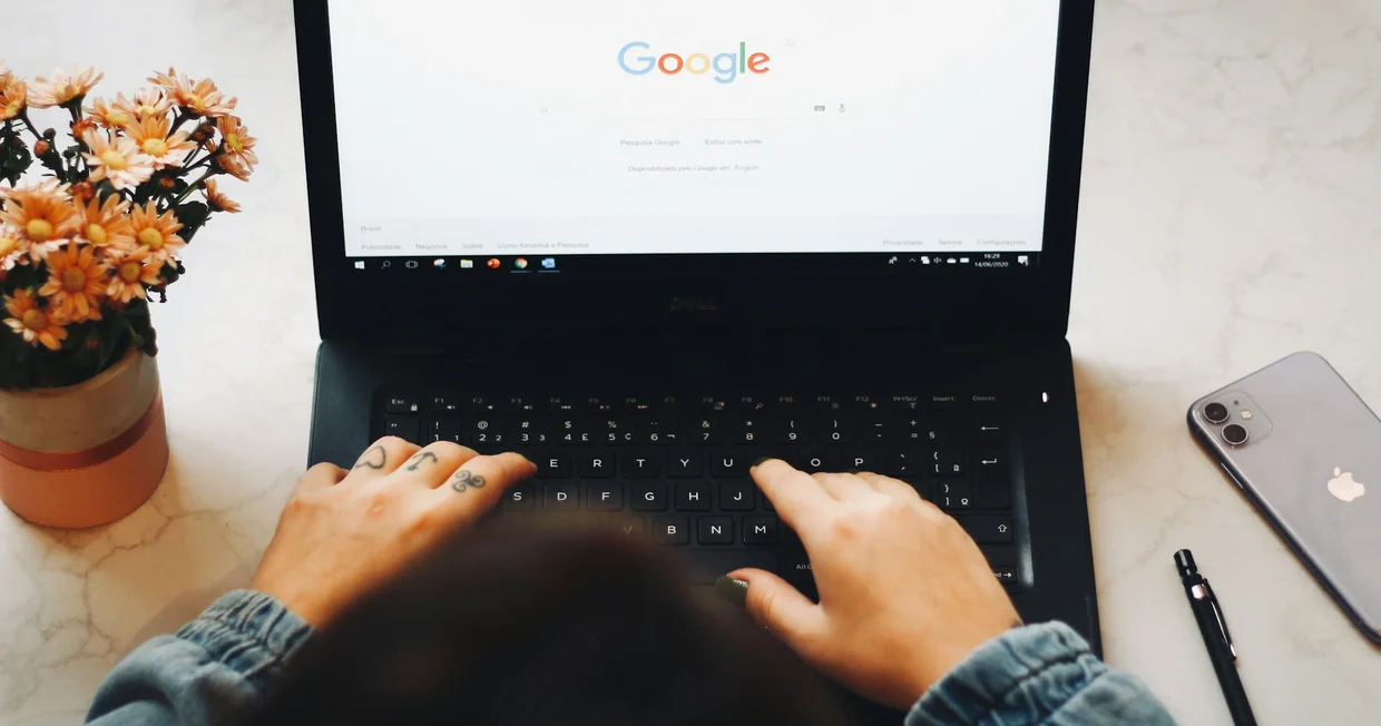 Hands typing on a laptop keyboard with the Google search page open on the screen