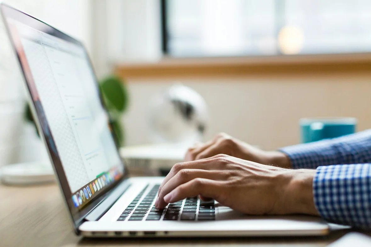 A person typing on a silver laptop at a bright desk