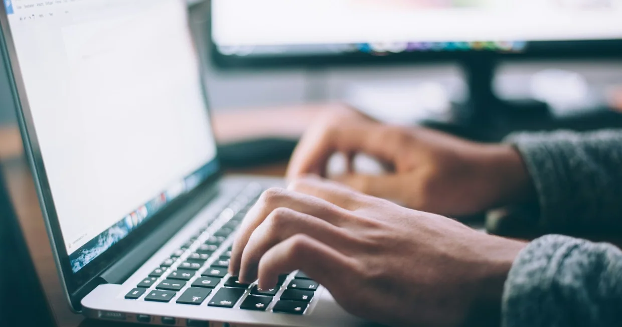 A person working on a laptop at a wooden desk