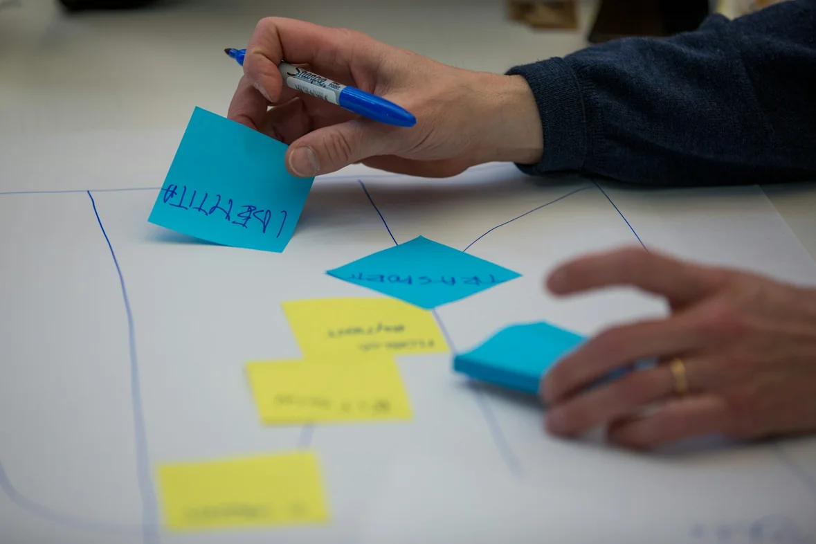 A hand writing in blue pen on white paper beside coloured sticky notes