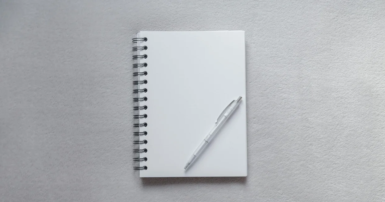 A blank spiral notebook lying open on a plain surface with a pen resting on the page