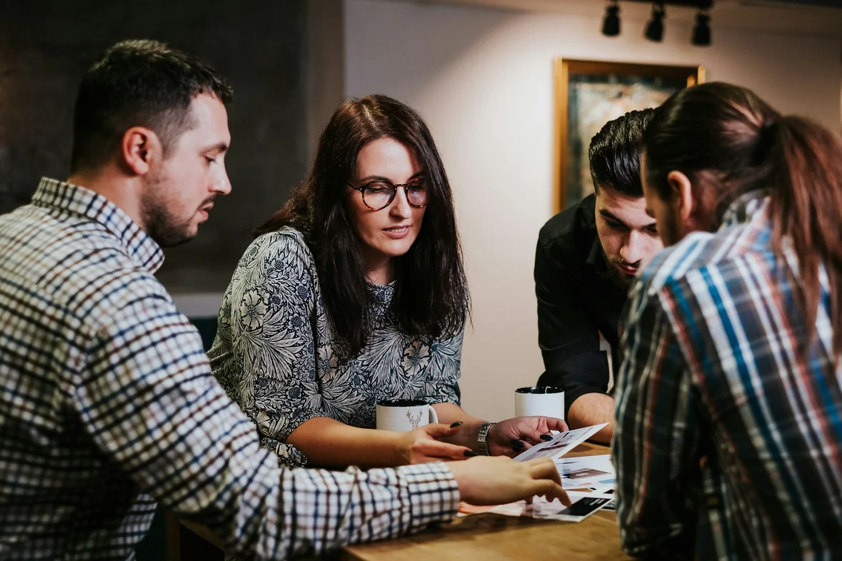 Four colleagues in conversation around a wooden table with coffee cups and printed documents in front of them