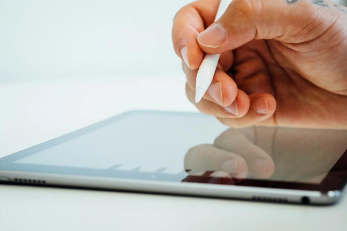 A hand holding a white stylus poised over a tablet screen