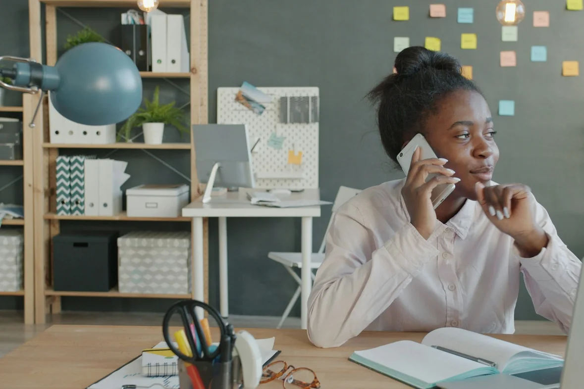 Someone taking a call at a desk beside an open laptop and a notebook
