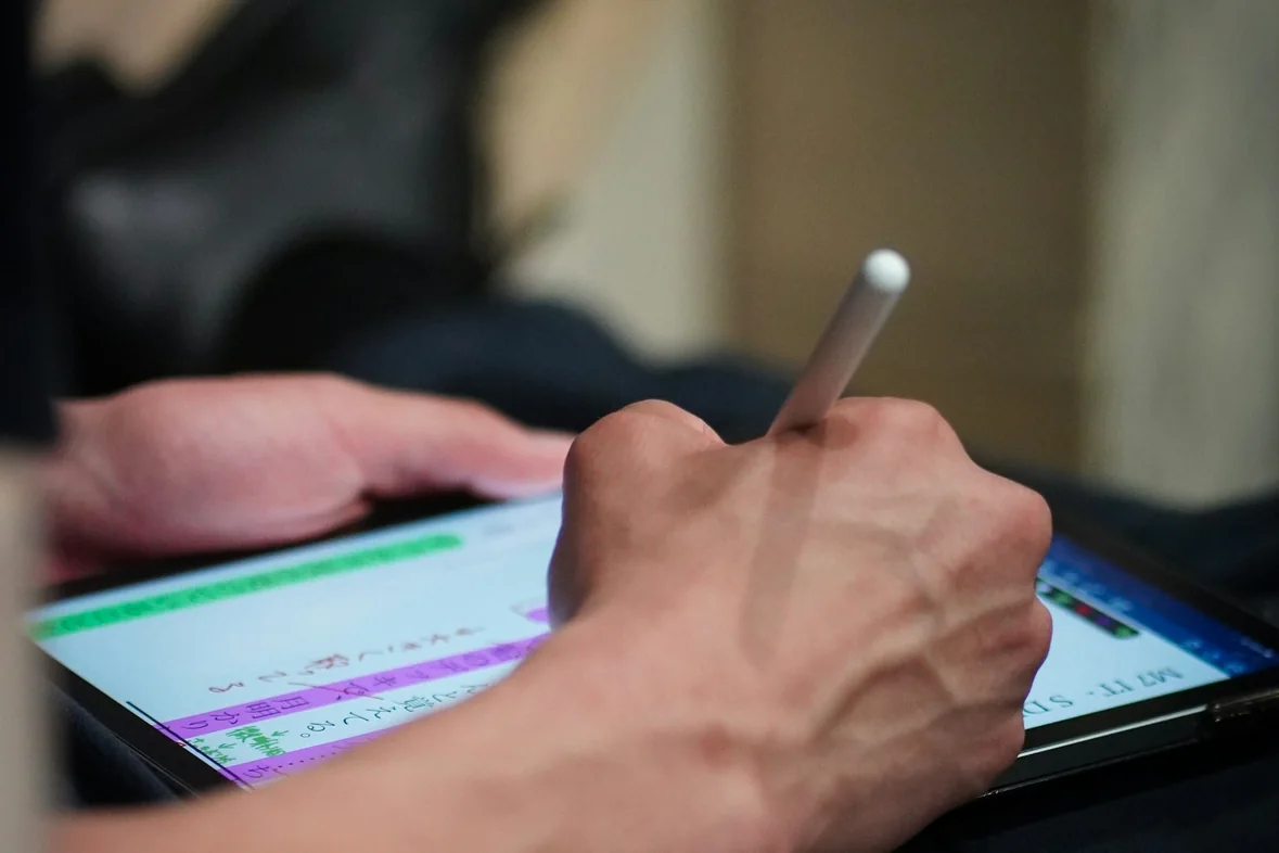 A hand using a stylus on a tablet showing a coloured scheduling interface