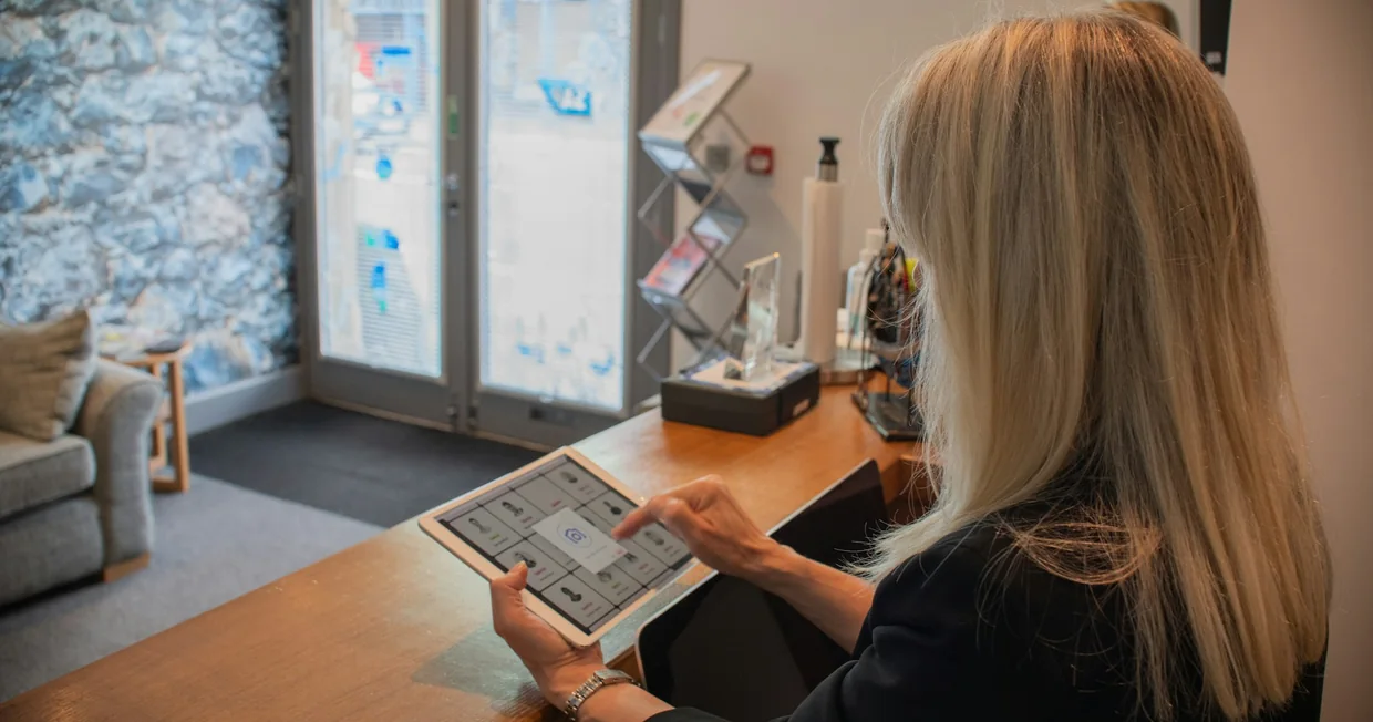 A person standing at a reception desk using a tablet, the office bright behind them