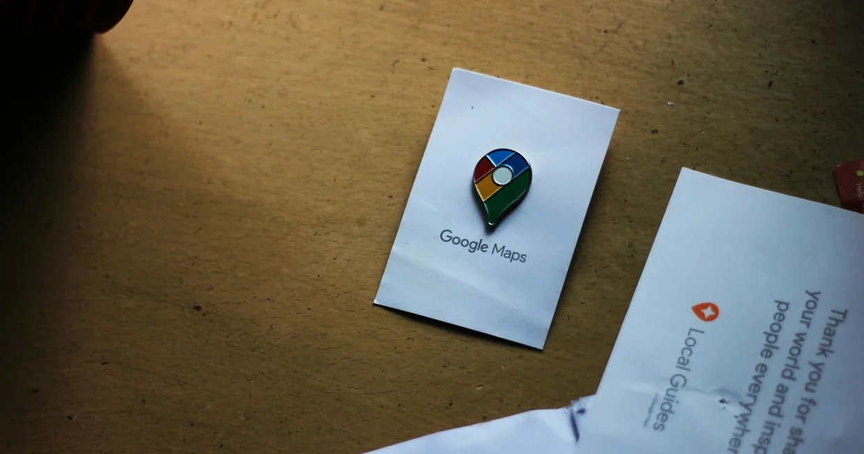 A Google Maps location pin printed on a card lying on a wooden desk beside a folded Local Guides letter
