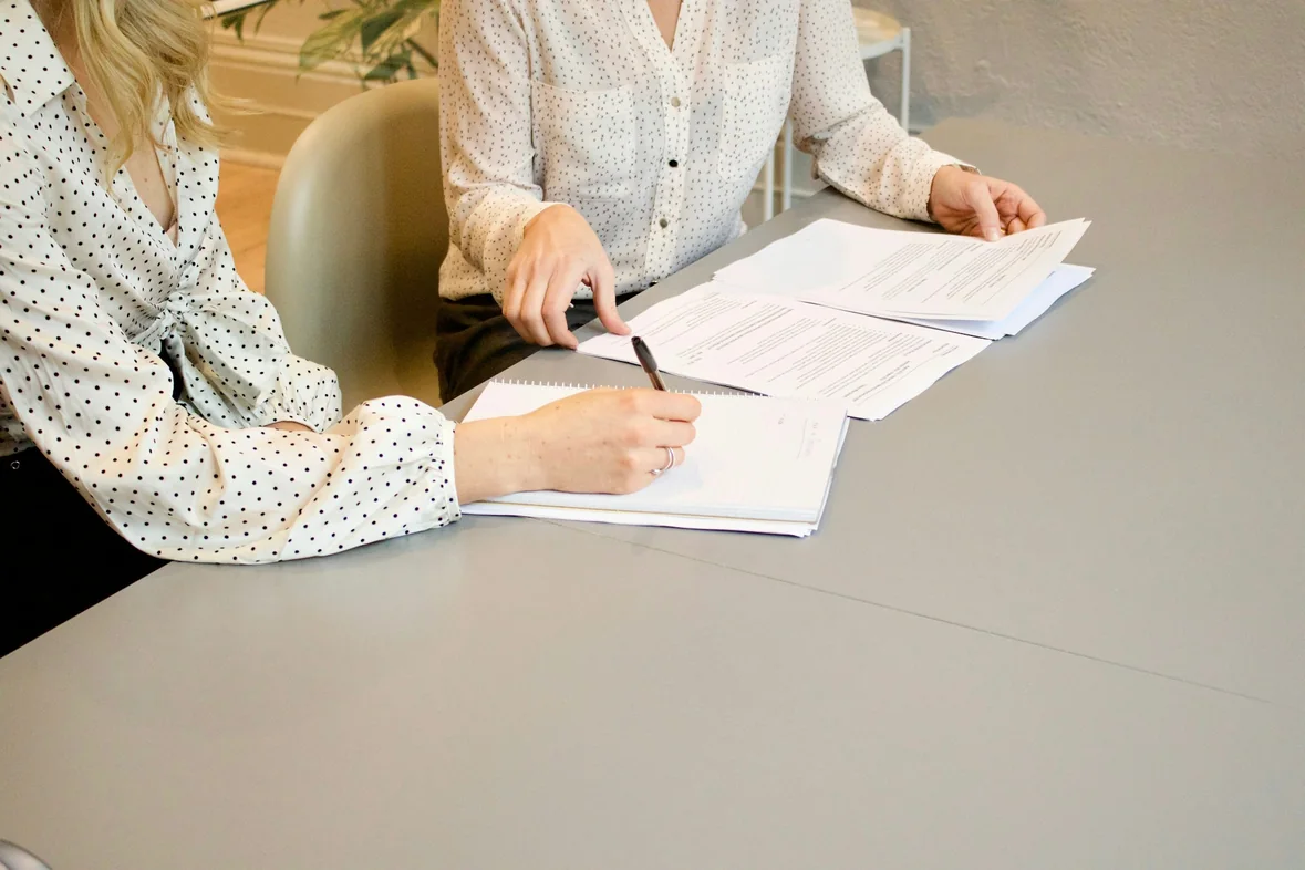 Two people at a table reviewing and signing a printed multi-page document