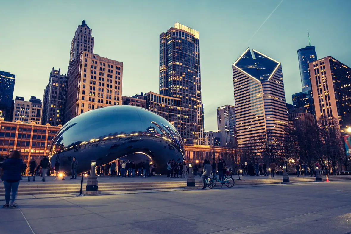 People gathered around a large reflective sculpture in a downtown Chicago plaza