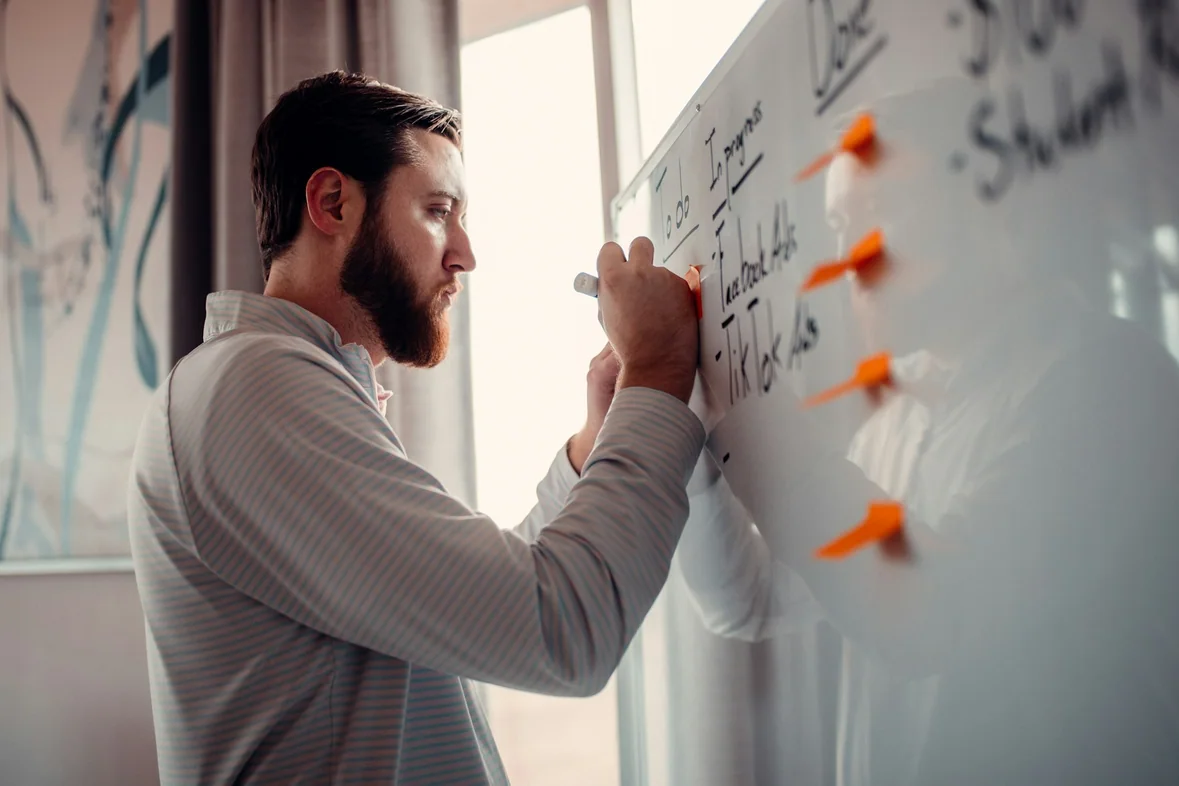 A man writing on a whiteboard with an orange marker pen