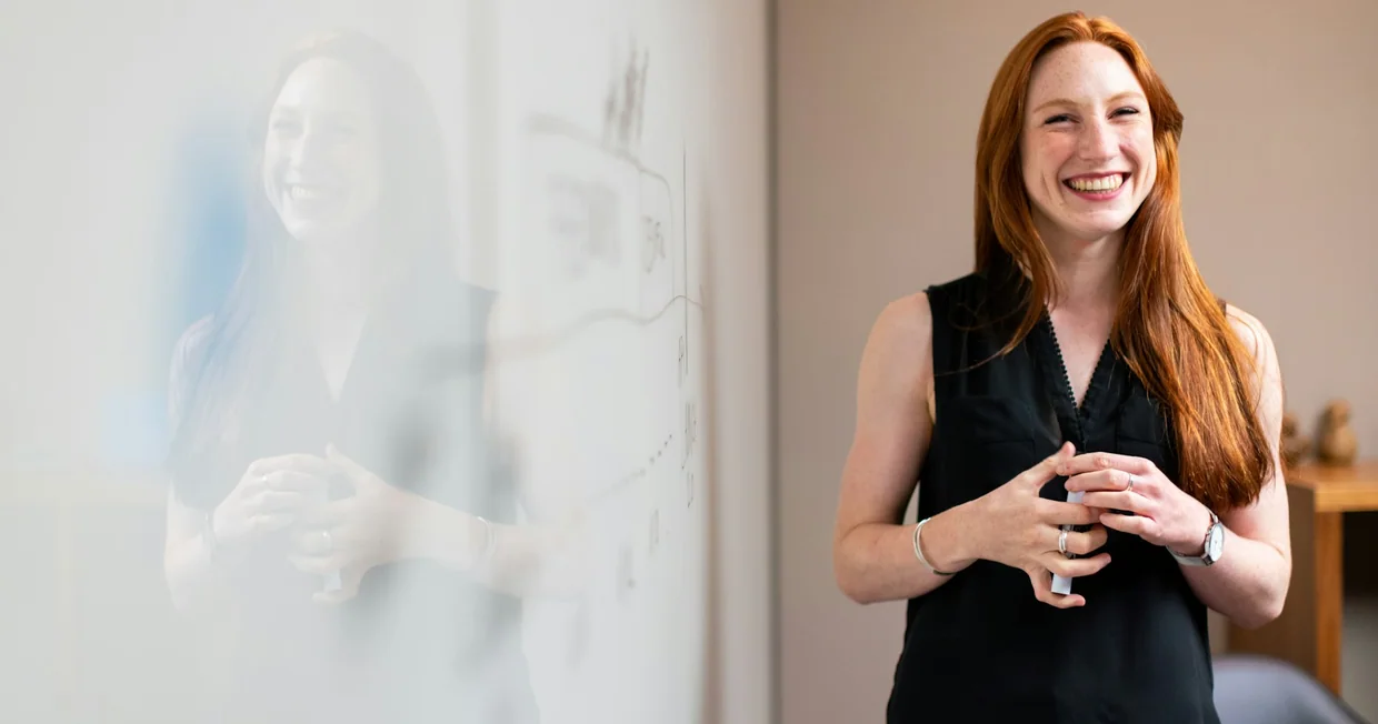 A woman presenting at a whiteboard, explaining something to colleagues out of shot