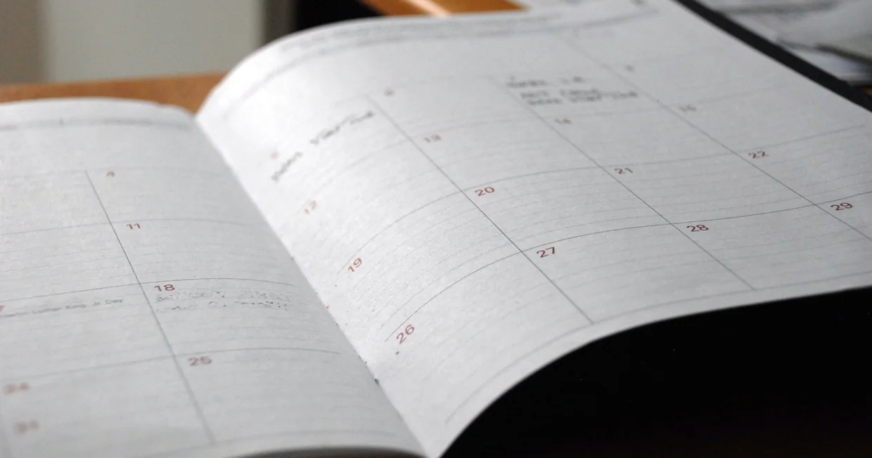 An open monthly planner lying on a wooden desk