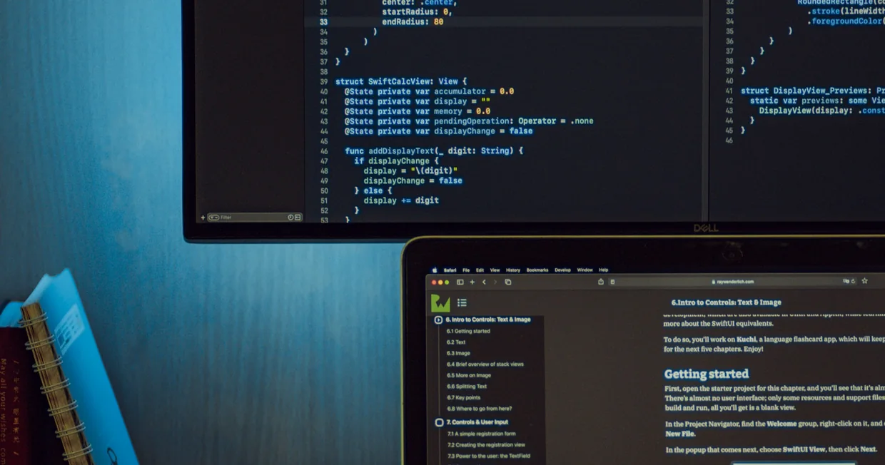 Two screens on a desk, one showing lines of code and the other a page of technical documentation