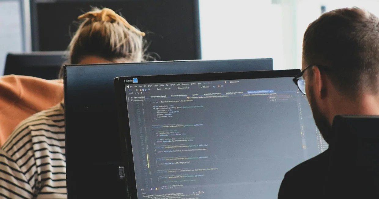 Two colleagues working side by side at desktop monitors in a shared office