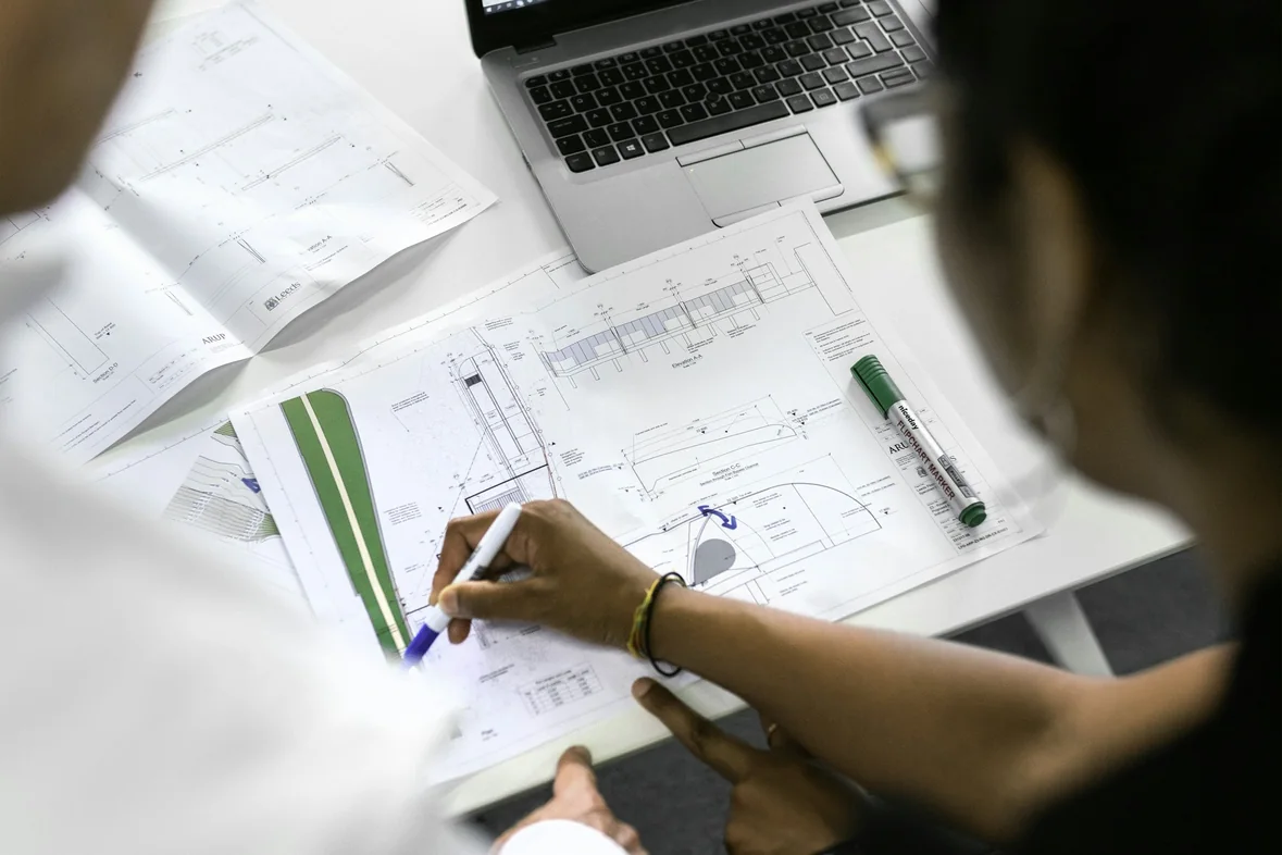 Someone sketching a page structure diagram in pen on a large sheet of paper next to an open laptop