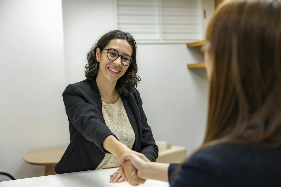 Two professionals shaking hands across a table in a bright meeting room