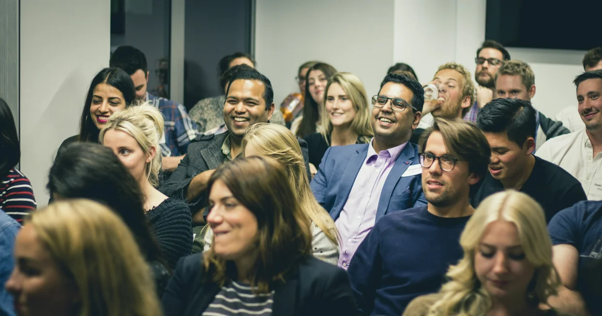 A crowded professional networking event, people standing in conversation groups and listening