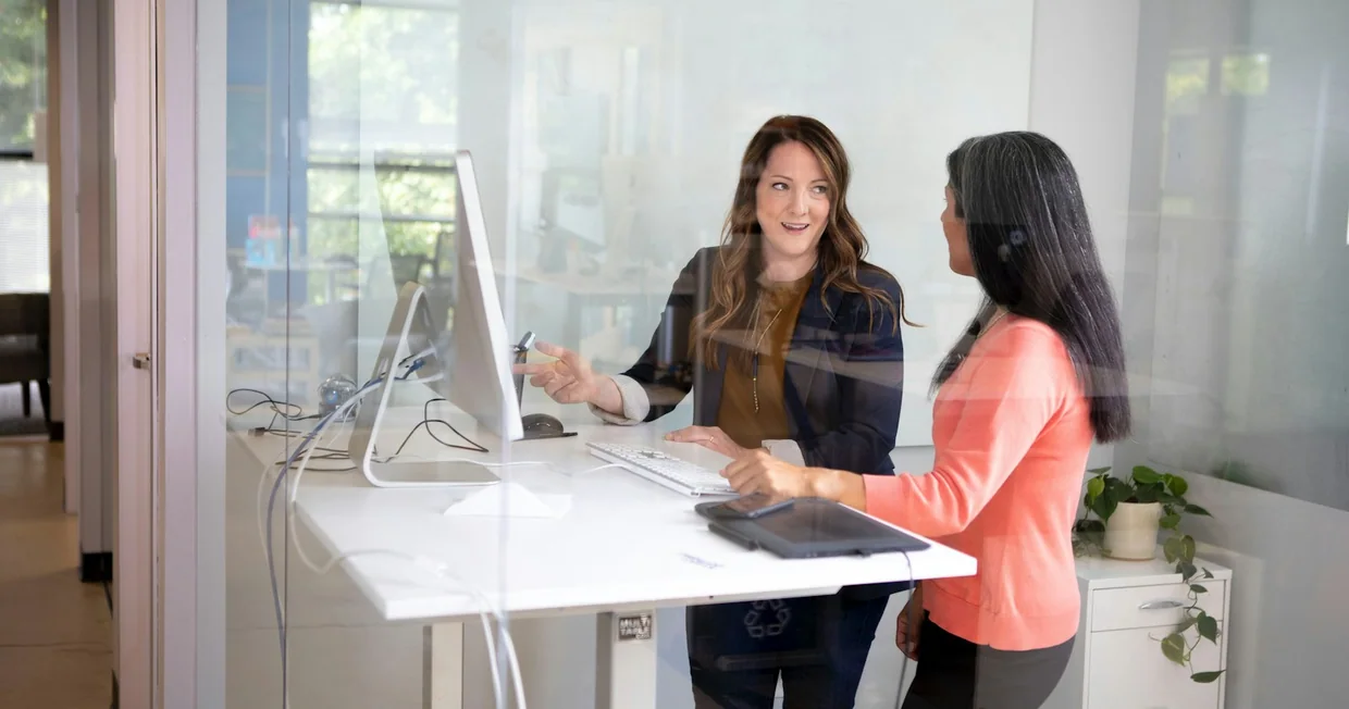 Two colleagues talking at a standing desk in a glass-walled office