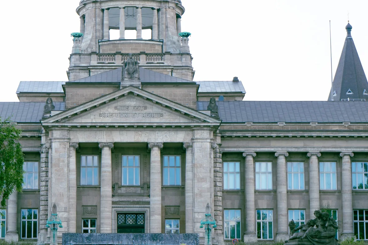 A large civic building with a green dome and figures walking past