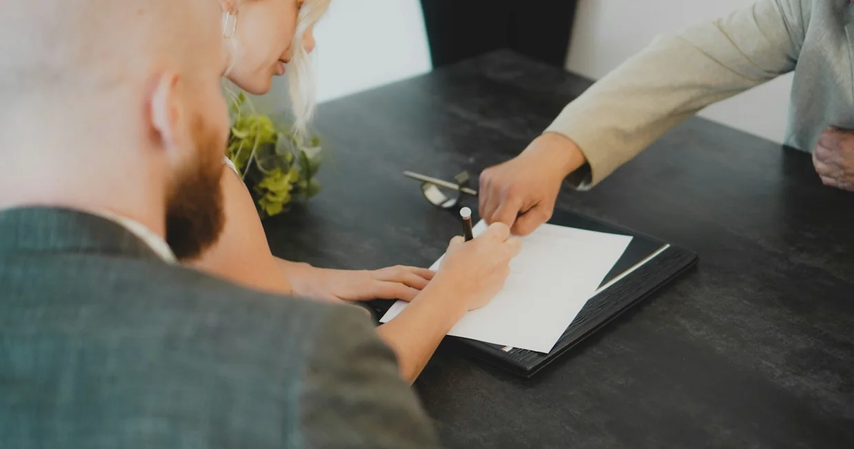 Two people at a desk signing a printed document together